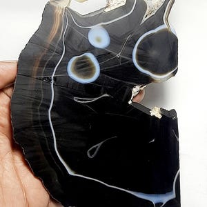 May include: A black agate slice with white and light blue banding. The agate has a unique, irregular shape with a hole in the center.