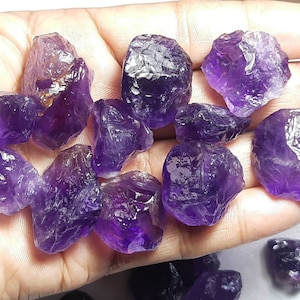 May include: A collection of raw amethyst crystals in various sizes and shapes. The crystals are a deep purple colour and have a natural, rough texture.