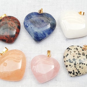 May include: Six heart-shaped pendants made of different types of stones, each with a gold bail. The stones include red jasper, blue sodalite, white quartz, pink rose quartz, and dalmatian jasper.