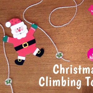 May include: A printable Christmas climbing toy featuring a Santa Claus character with a red suit, white beard, and black belt. The toy is attached to two strings with green star-shaped pieces at the bottom.