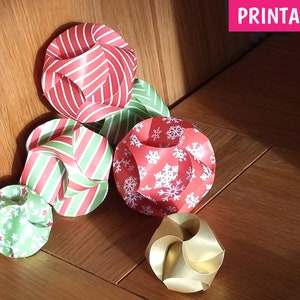 Puede incluir: Cinco adornos de papel en varios patrones. Los adornos son de rayas rojas y blancas, de rayas verdes y blancas, rojos con copos de nieve blancos, verdes con estrellas blancas y dorados. Los adornos est&aacute;n sobre una superficie de madera. IMPRIMIBLE.
