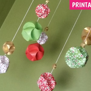 Puede incluir: Adornos de papel imprimibles en varios colores y patrones, incluyendo rojo, verde, dorado y blanco. Los adornos cuelgan de cuerdas y presentan diferentes dise&ntilde;os, como estrellas, lunares y formas geom&eacute;tricas. La palabra "IMPRIMIBLE" es visible en la esquina superior derecha de la imagen.