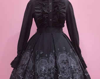 May include: Black and white lolita dress with a high collar and ruffled sleeves. The skirt features a print of white flowers and geometric shapes on a black background. The dress has a black lace trim.