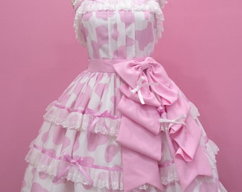 Puede incluir: Un vestido lolita de estampado de vaca rosa y blanco con un gran lazo rosa y ribete de encaje. El vestido está en un maniquí sobre un fondo rosa. El texto "Glitter Tale custom size Lolita fashion" está en la parte inferior de la imagen.