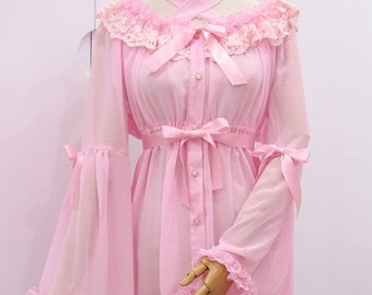 May include: A pink sheer blouse with long sleeves and a lace trim. The blouse has a button-up front and a bow at the waist. The sleeves have a ruffle at the cuff and a bow at the wrist.