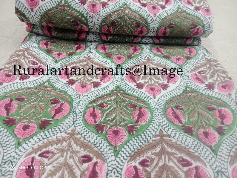 Pu&ograve; includere: Tessuto di cotone bianco con un motivo ripetitivo di fiori rosa e marroni e foglie verdi. Il tessuto &egrave; piegato a met&agrave; e il testo "Ruralartandcrafts@Image" &egrave; visibile.