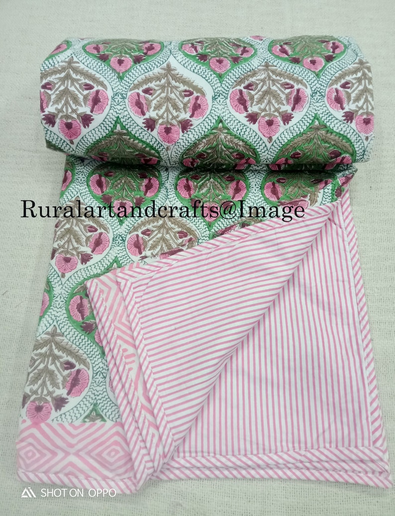 Pu&ograve; includere: Un trapunta di cotone rosa e verde con un motivo floreale su un lato e strisce rosa e bianche sull'altro. La trapunta &egrave; piegata a met&agrave; e il lato floreale &egrave; rivolto verso l'alto.