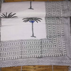 May include: White cotton fabric with a black and white palm tree print. The fabric has a gray and white border with a wavy pattern.