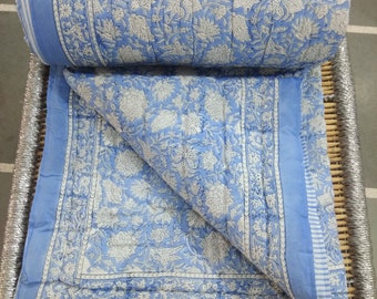 May include: A blue and white floral patterned cotton quilt with a white border. The quilt is folded in half and is sitting on a woven bamboo mat.