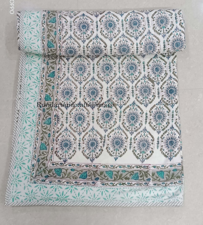 May include: White cotton quilt with a blue and green floral pattern. The quilt has a border with a light blue and white star pattern.