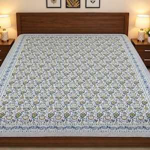 May include: A bedspread featuring a repeating floral pattern in shades of blue, green, and yellow on a white background. The central design is enclosed by a decorative border with a blue and white paisley motif, covering the entire bed surface.