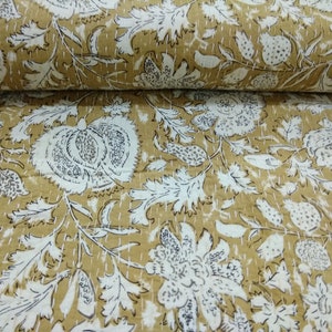 May include: A beige cotton fabric with a white floral pattern. The fabric is quilted and has a subtle sheen.