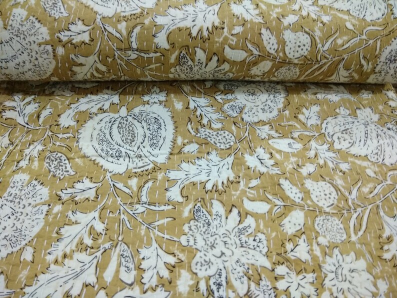 May include: A beige cotton fabric with a white floral pattern. The fabric is quilted and has a subtle sheen.