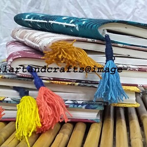 May include: A stack of four journals with colorful patterned covers and tassel bookmarks. The journals are arranged on a bamboo surface.