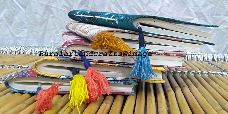 May include: A stack of four journals with colorful patterned covers and tassel bookmarks. The journals are arranged on a bamboo surface.