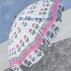 Op de afbeelding: Een witte en roze bloemenprint paraplu met een roze rand. De paraplu is gesloten en heeft een gerimpelde rand.