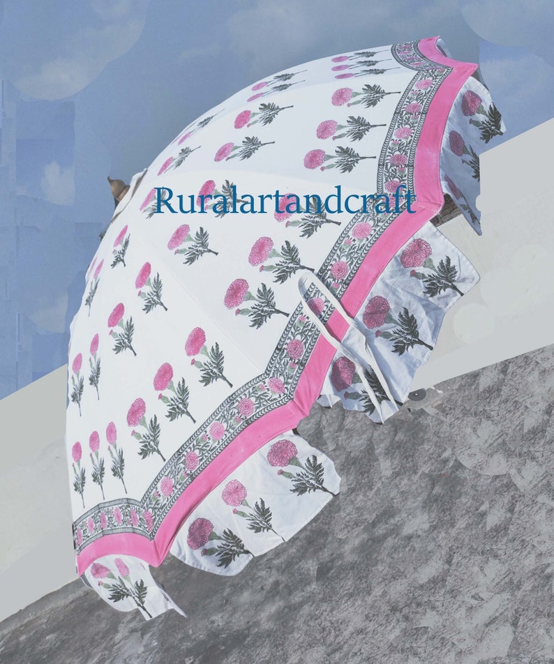 Op de afbeelding: Een witte en roze bloemenprint paraplu met een roze rand. De paraplu is gesloten en heeft een gerimpelde rand.