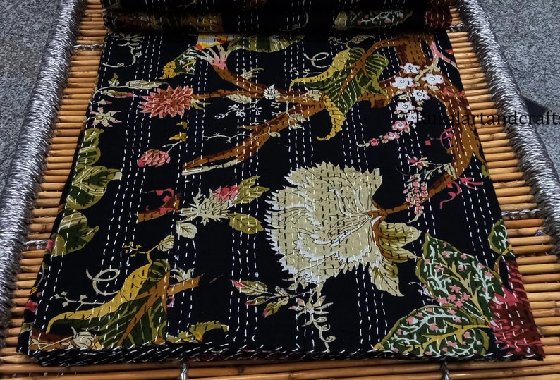 May include: Black kantha quilt with a floral pattern featuring white, green, and brown flowers. The quilt is hand-stitched with white thread and has a traditional Indian design.