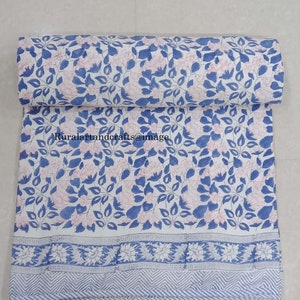 Op de afbeelding: Een witte stof met een blauwe en roze bloemenprint. De stof heeft een blauwe rand met een wit en blauw geometrisch patroon.