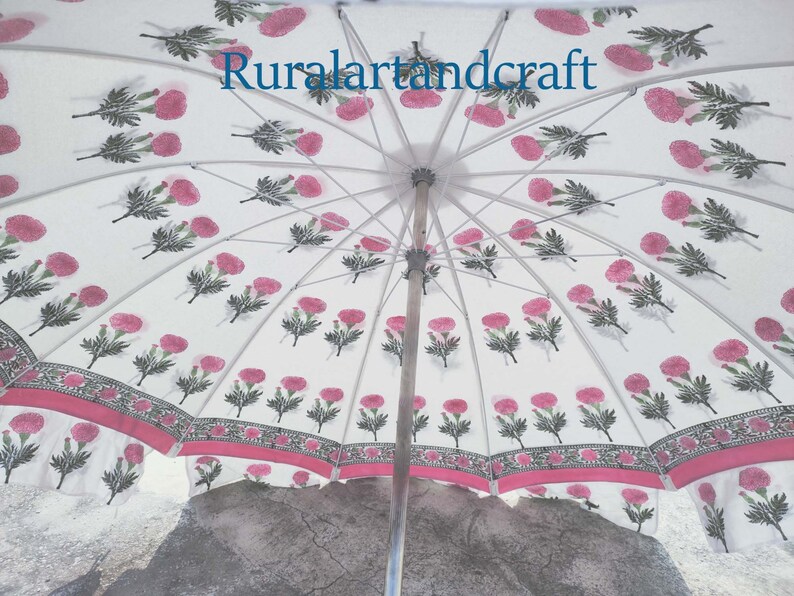 Op de afbeelding: Een witte paraplu met een roze en groene bloemenprint. De paraplu is open en de binnenkant van de kap is zichtbaar. De tekst "Ruralartandcraft" is op de paraplu gedrukt.