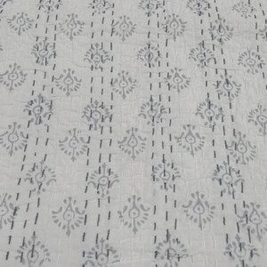 May include: White cotton fabric with a repeating pattern of small grey floral designs. The fabric is quilted with a running stitch.