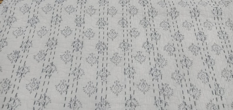 May include: White cotton fabric with a repeating pattern of small grey floral designs. The fabric is quilted with a running stitch.
