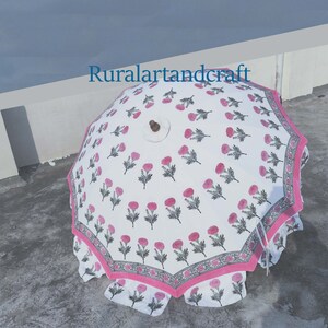 Op de afbeelding: Een witte en roze bloemenprint paraplu met een houten handvat. De paraplu is open en de stof is bedrukt met roze bloemen en groene bladeren. De paraplu heeft een roze en witte rand.
