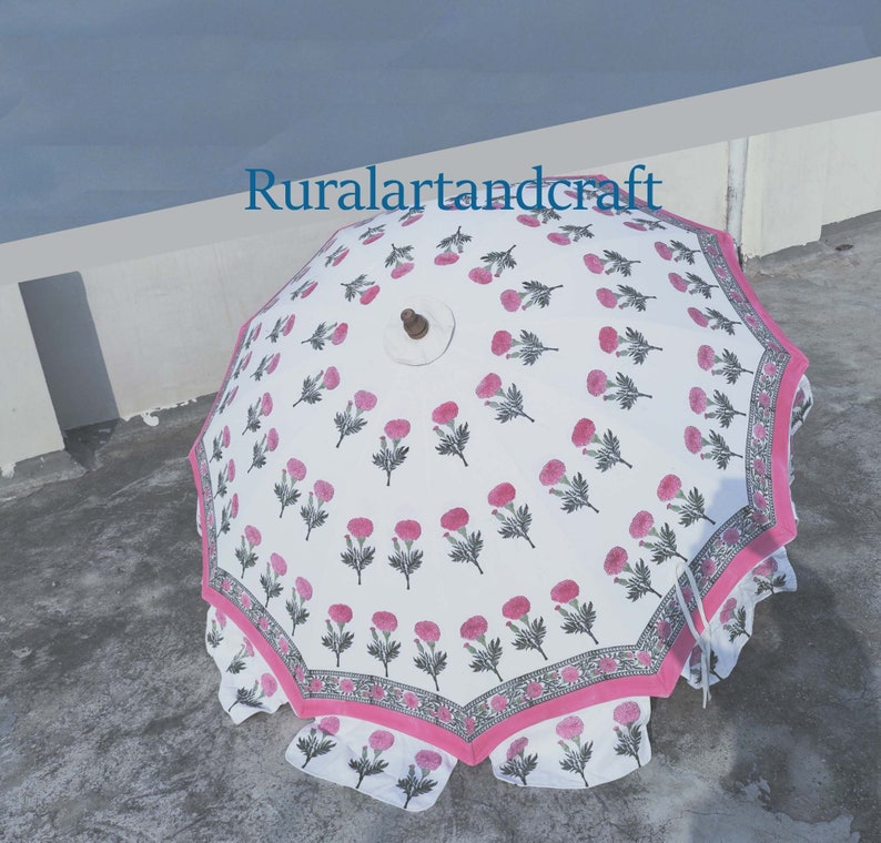Op de afbeelding: Een witte en roze bloemenprint paraplu met een houten handvat. De paraplu is open en de stof is bedrukt met roze bloemen en groene bladeren. De paraplu heeft een roze en witte rand.