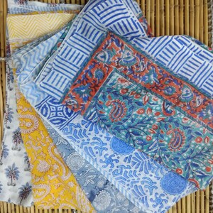 May include: Four cotton scarves with different floral and geometric patterns in shades of blue, red, yellow, and white. The scarves are folded and arranged on a bamboo surface.