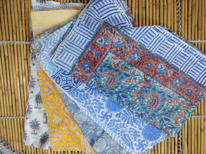 May include: Four cotton scarves with different floral and geometric patterns in shades of blue, red, yellow, and white. The scarves are folded and arranged on a bamboo surface.