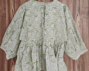 Op de afbeelding: Een lichtgroene en witte blouse met een uniek tijgerstreepmotief. De blouse heeft lange mouwen en een gefranjerde zoom. Het hangt aan een houten hanger tegen een houten achtergrond.