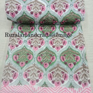 Pu&ograve; includere: Tessuto di cotone bianco con stampa floreale rosa e verde. Il tessuto presenta un motivo ripetitivo di fiori e foglie stilizzati. Il tessuto &egrave; piegato a met&agrave; e i bordi sono visibili.