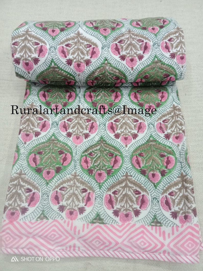 Pu&ograve; includere: Tessuto di cotone bianco con stampa floreale rosa e verde. Il tessuto presenta un motivo ripetitivo di fiori e foglie stilizzati. Il tessuto &egrave; piegato a met&agrave; e i bordi sono visibili.