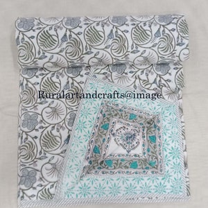 May include: A white cotton quilt with a floral print in shades of gray and green. The quilt is folded in half and has a decorative border with a blue and green pattern.