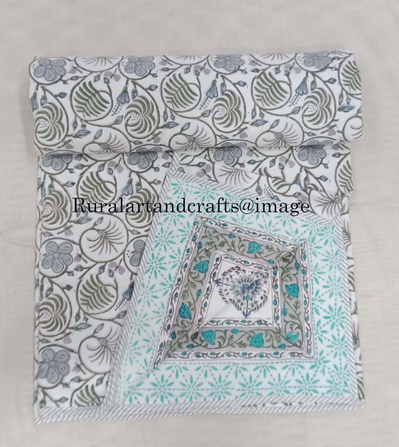 May include: A white cotton quilt with a floral print in shades of gray and green. The quilt is folded in half and has a decorative border with a blue and green pattern.