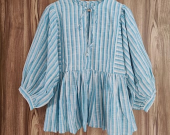 Op de afbeelding: Een blauw-wit gestreepte blouse met driekwart mouwen en een geplooid taille. De blouse heeft een V-hals met een striksluiting en hangt aan een houten kleerhanger.