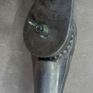 Op de afbeelding: Een verstelbare ondersteuning van zilverkleurig metaal met een draaiknop en een tandwielmechanisme. De ondersteuning is ontworpen om aan een paal of andere constructie te worden bevestigd.