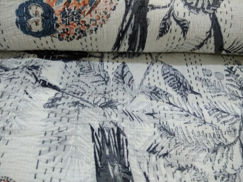 May include: A white kantha quilt with a black and gray floral pattern. The quilt is hand-stitched and has a soft, textured surface.