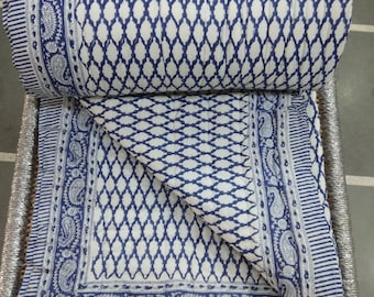 Könnte beinhalten: Eine weiße und blaue Baumwolldecke mit geometrischem Muster und Paisley-Bordüre. Die Decke ist gefaltet und auf einem geflochtenen Korb ausgestellt.