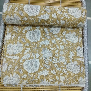 May include: A yellow and white kantha quilt with a floral pattern. The quilt is folded and rolled up on a woven bamboo mat.