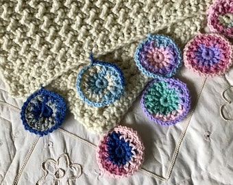 Könnte beinhalten: Eine weiße Häkeldecke mit bunten Häkelblumen, die am Rand befestigt sind. Die Blumen sind in den Farben Rosa, Blau, Grün und Lila.