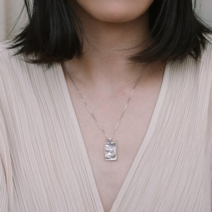 Pode incluir: Uma mulher com cabelo preto curto vestindo uma blusa bege claro com um colar de prata e um pingente de prata texturizado.