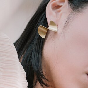 May include: A pair of gold-toned earrings with a twisted, abstract design. The earrings are made of metal and have a polished finish.
