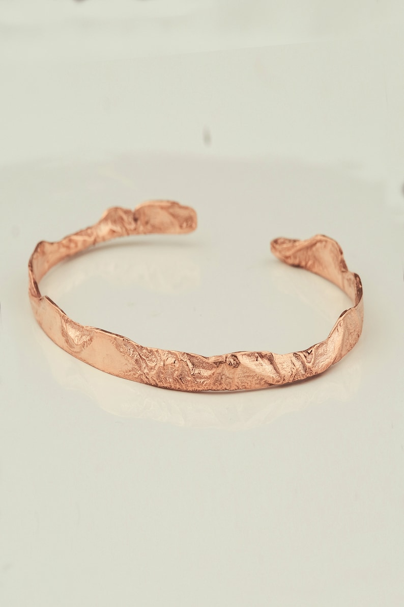 May include: A rose gold textured metal bangle bracelet. The bracelet is open and has a hammered finish.