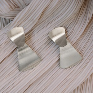 May include: A pair of silver geometric earrings with a unique, asymmetrical design. The earrings are made of a smooth, metallic material and have a modern, minimalist aesthetic.
