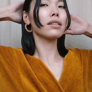 May include: A woman with dark hair wearing a mustard yellow velvet robe and gold hoop earrings.