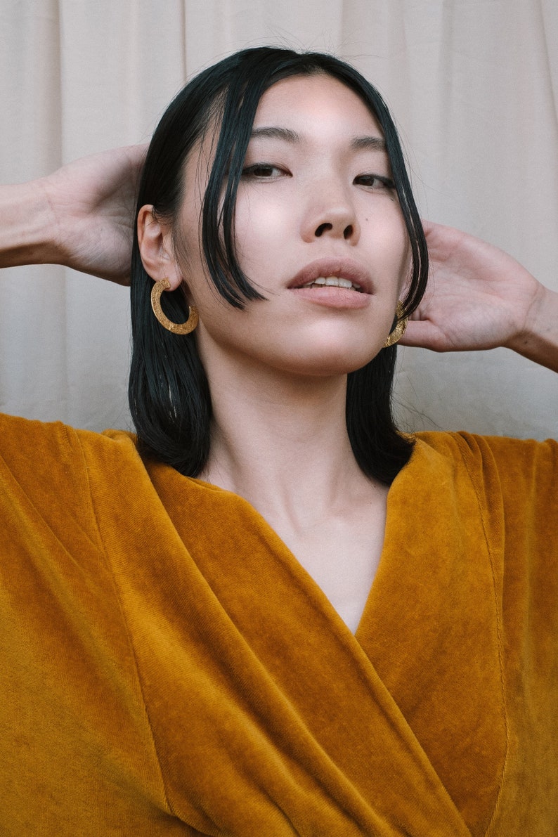 May include: A woman with dark hair wearing a mustard yellow velvet robe and gold hoop earrings.