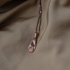 Peut inclure: Un collier d&eacute;licat en or rose avec un pendentif en forme de larme textur&eacute;. Le pendentif a une finition martel&eacute;e et pend &agrave; une cha&icirc;ne d&eacute;licate.