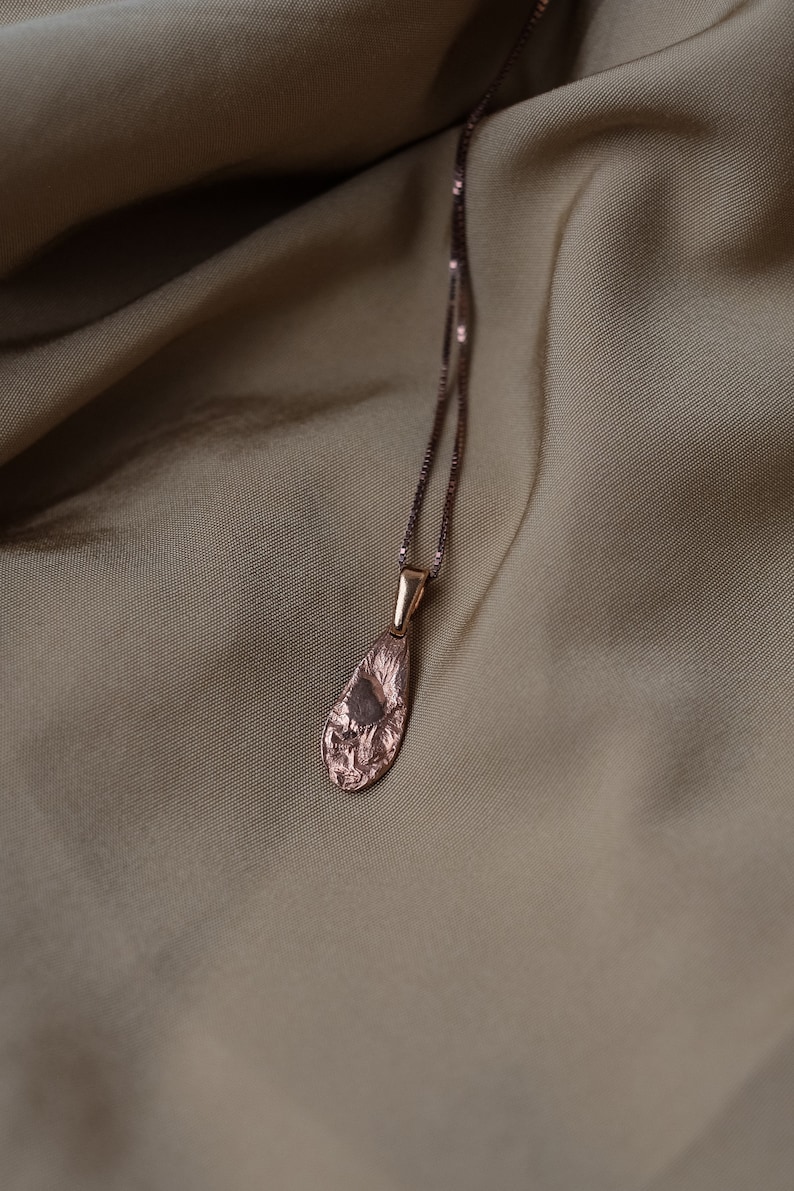 Peut inclure: Un collier d&eacute;licat en or rose avec un pendentif en forme de larme textur&eacute;. Le pendentif a une finition martel&eacute;e et pend &agrave; une cha&icirc;ne d&eacute;licate.