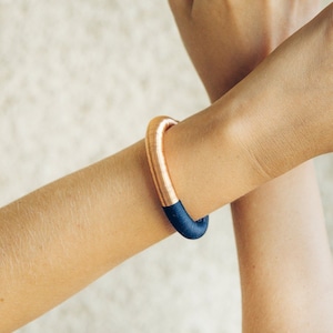 Pu&ograve; includere: Un braccialetto rigido in rame e blu scuro. Il braccialetto &egrave; realizzato con un sottile filo di rame avvolto attorno a una fascia blu scuro.